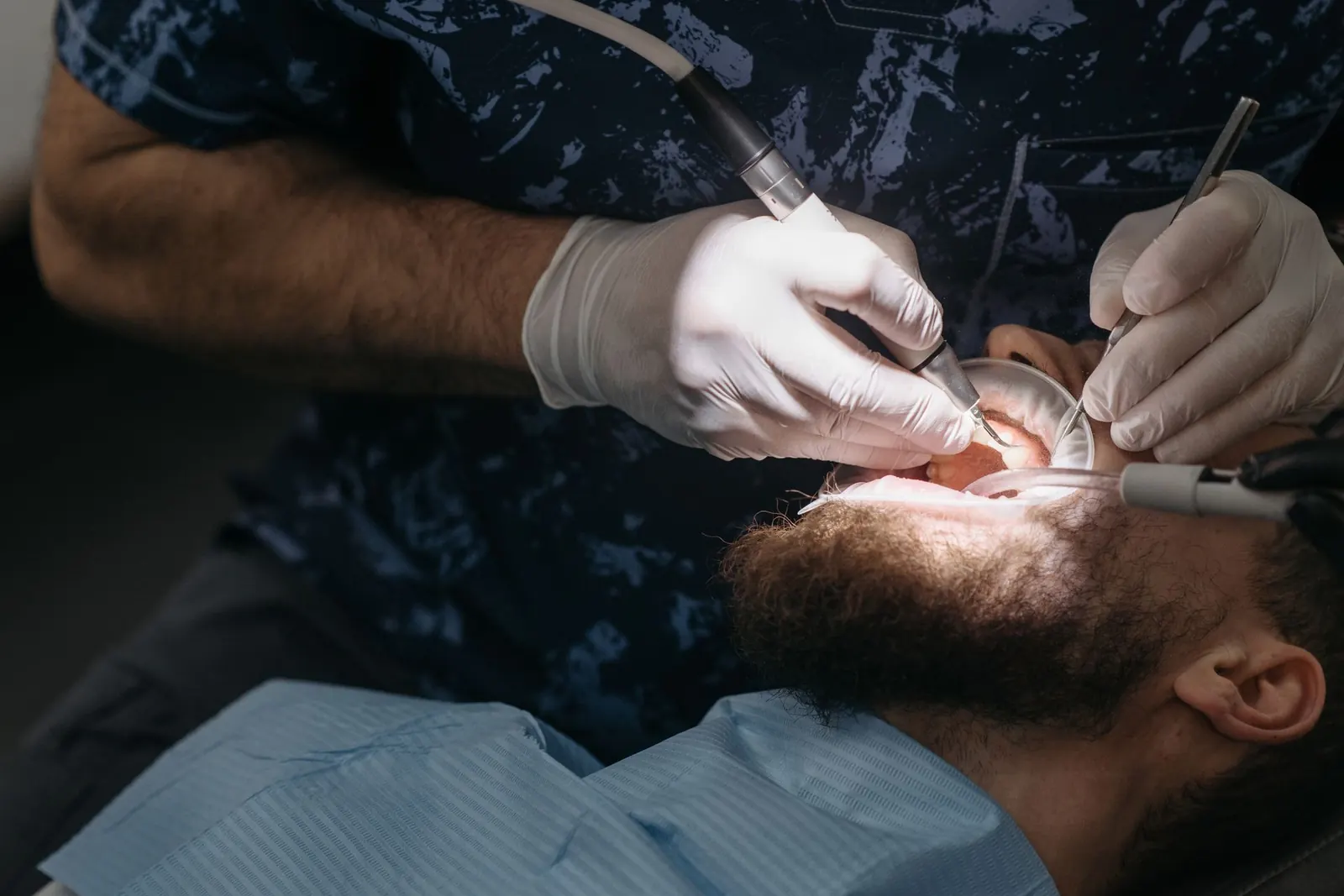 Dr. Rowe at work: a dentist in scrubs treating a patient under calm, focused clinical light