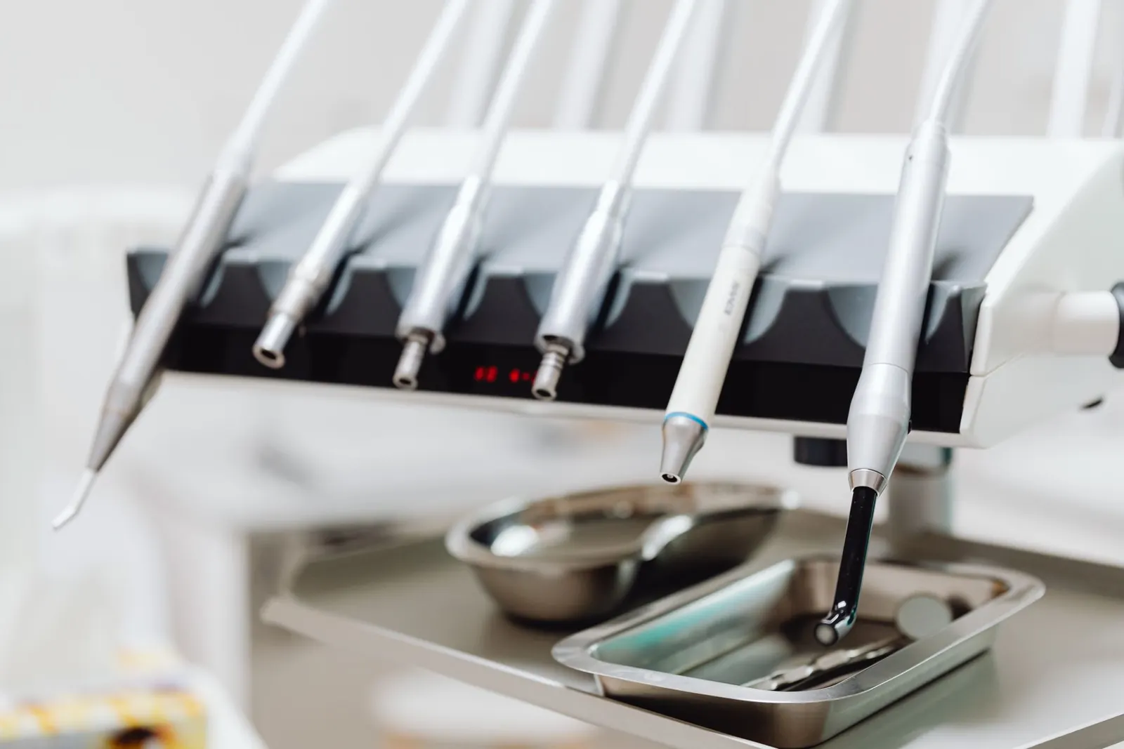Close-up of polished dental handpieces docked above two stainless-steel instrument trays