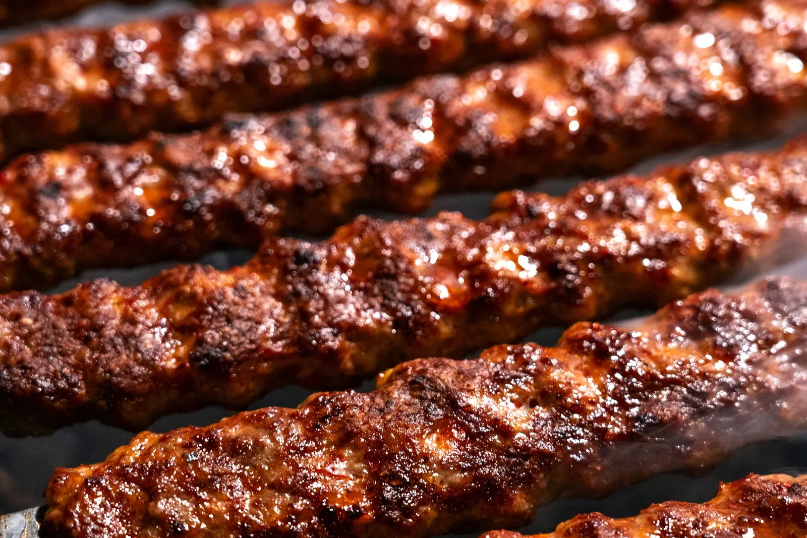Rows of hand-ground kofta kebabs on flat metal skewers, glossy and deeply charred from the grill