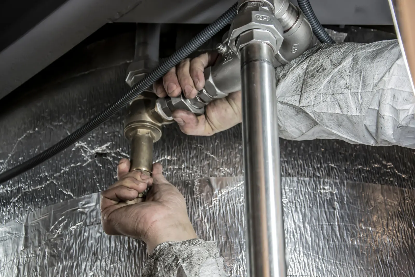 A plumber in work coveralls making up a threaded pipe fitting by hand
