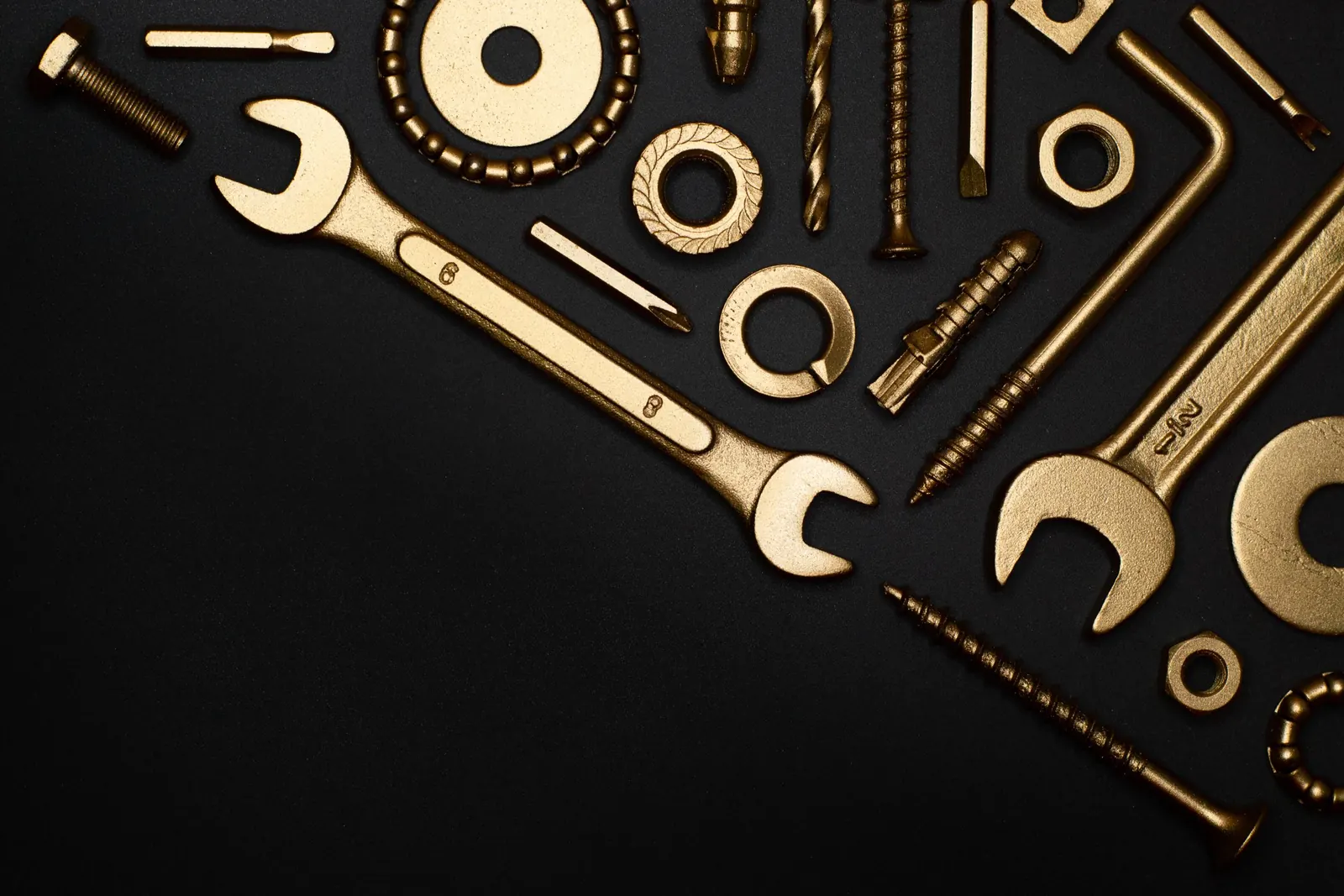 Wrenches, drill bits, washers, and fasteners laid out on a dark workbench
